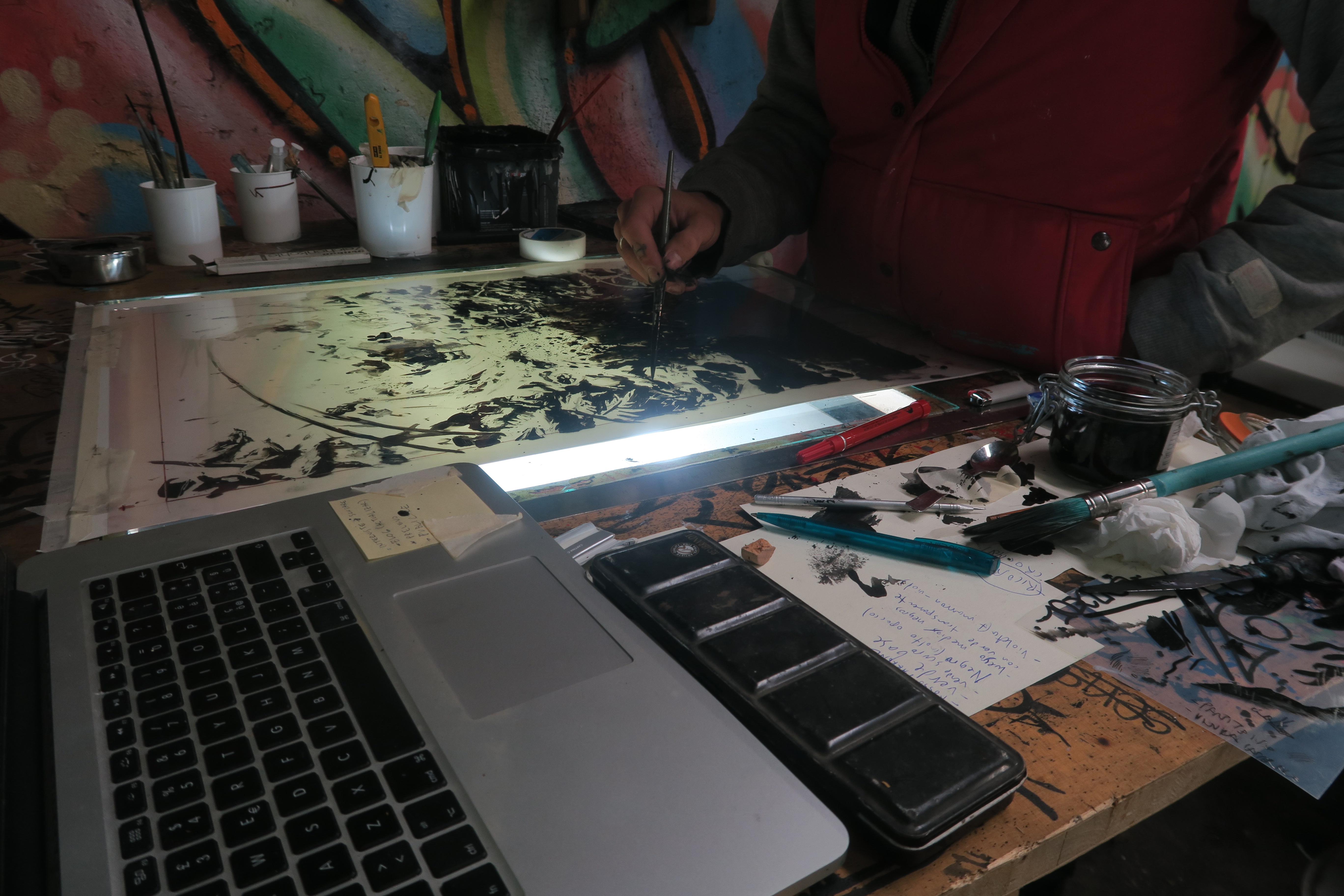 Artista al lavoro nel suo studio con laptop, inchiostri e opere d'arte